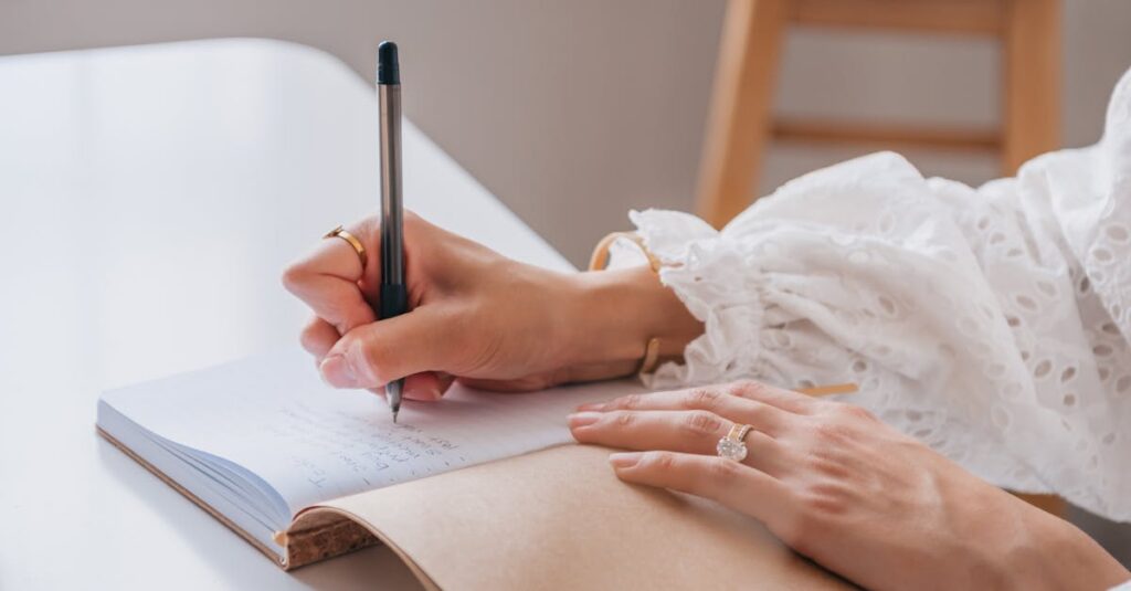 Close-up of a woman writing in a notebook at a bright home office desk.