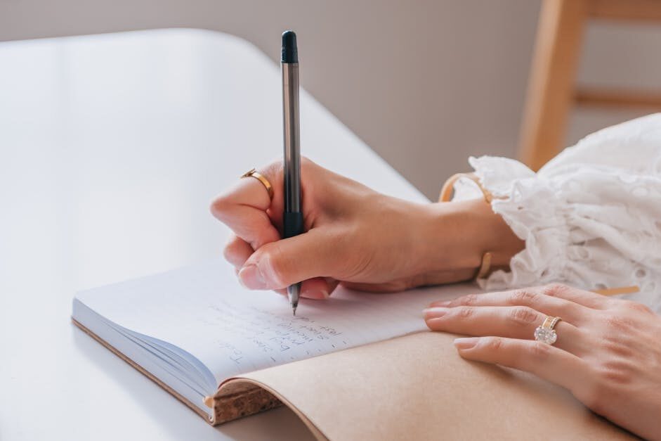 Close-up of a woman writing in a notebook at a bright home office desk.